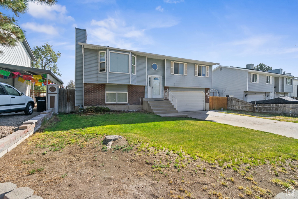 Bi-level home with a chimney, brick siding, an attached garage, and driveway