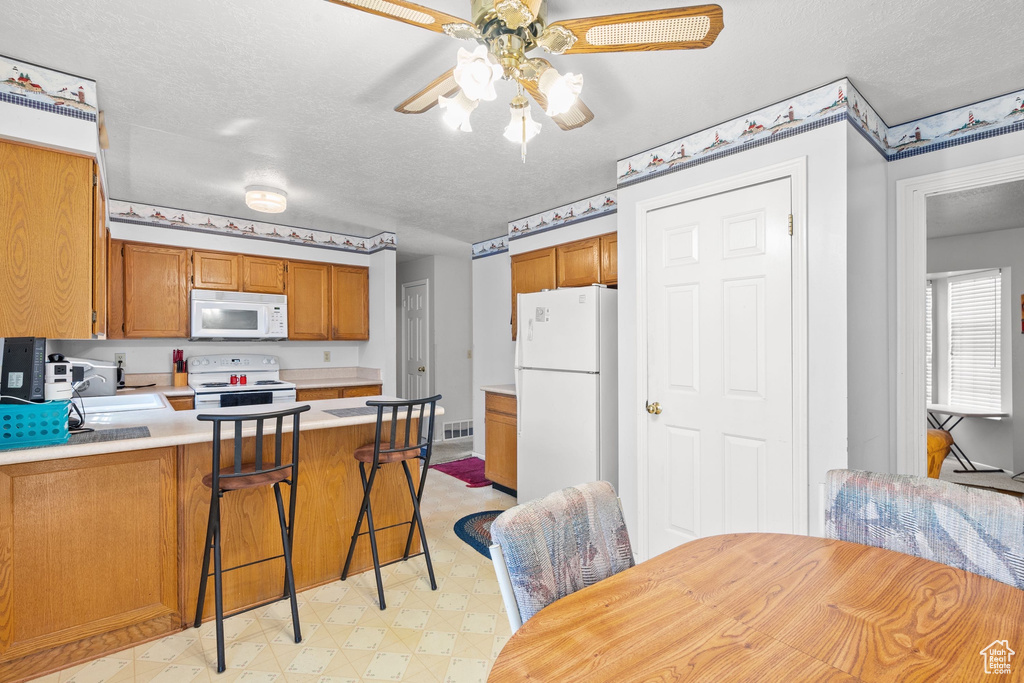 Kitchen featuring white appliances, light floors, a peninsula, light countertops, and brown cabinets