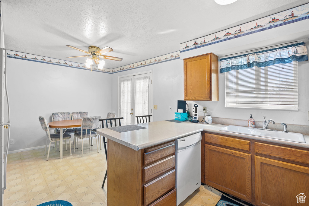 Kitchen featuring dishwasher, a peninsula, light flooring, a ceiling fan, and a sink