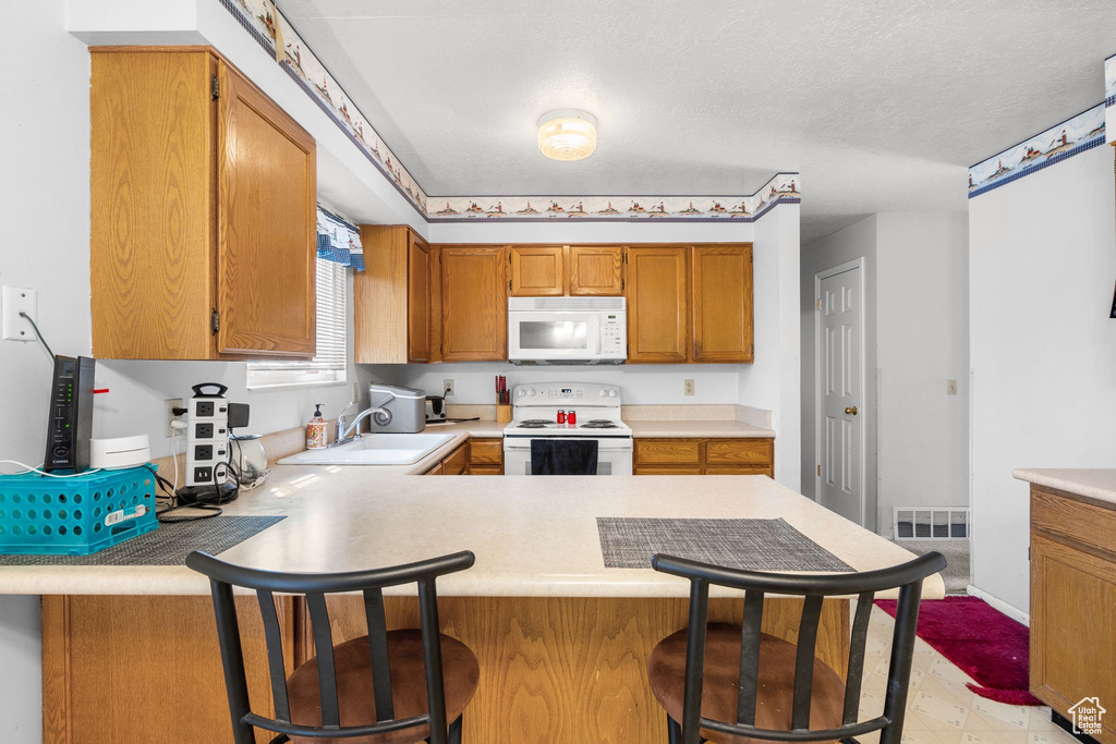 Kitchen featuring white appliances, a sink, a peninsula, and light countertops
