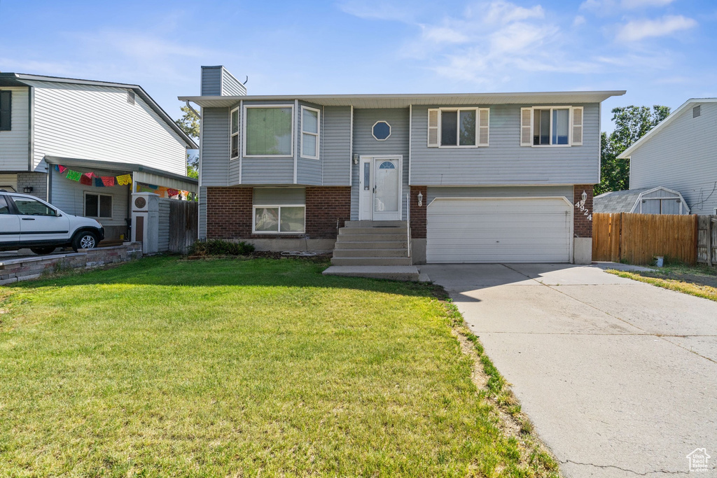 Bi-level home with an attached garage, brick siding, a chimney, and concrete driveway