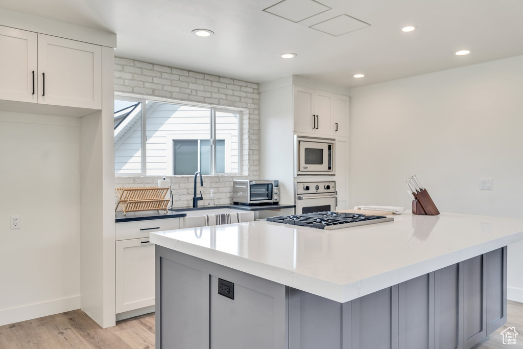 Kitchen featuring oven, a sink, stainless steel microwave, light wood finished floors, and a kitchen island