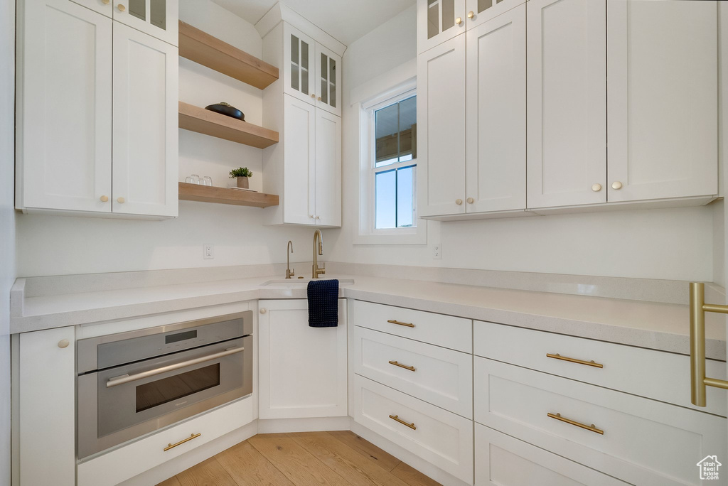 Kitchen featuring oven, open shelves, white cabinets, light countertops, and light wood-style floors