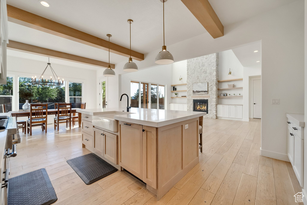Kitchen featuring light brown cabinets, a sink, a stone fireplace, open floor plan, and beam ceiling
