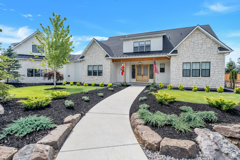 Modern farmhouse with stone siding, a porch, and a front yard