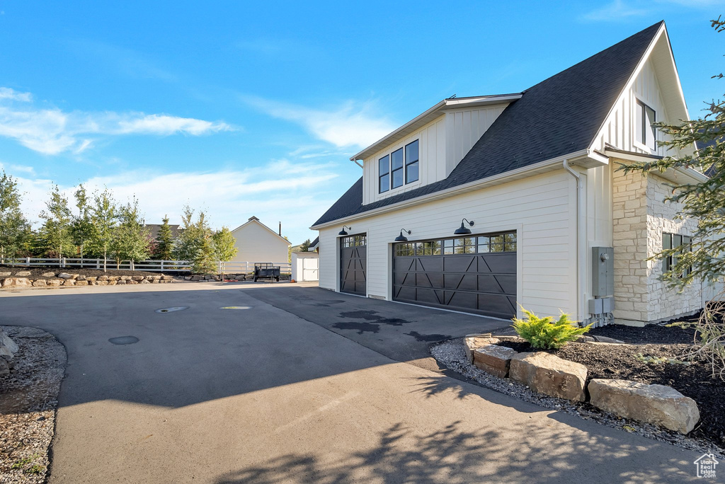 View of side of home with driveway, a shingled roof, board and batten siding, and an attached garage