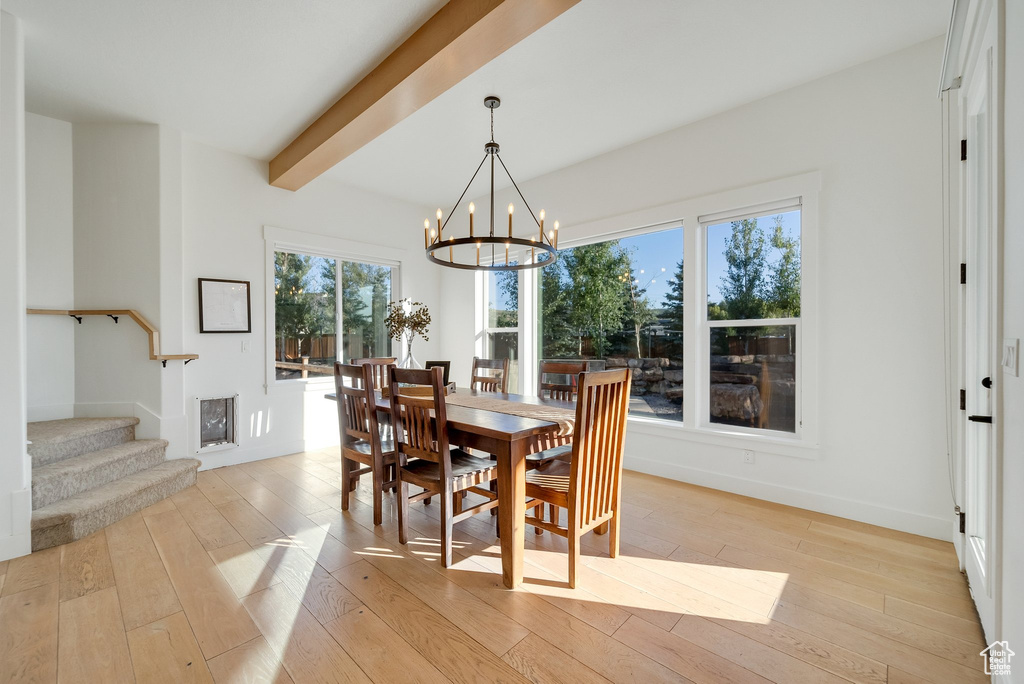 Dining space with light wood-style flooring, a chandelier, stairs, beamed ceiling, and baseboards