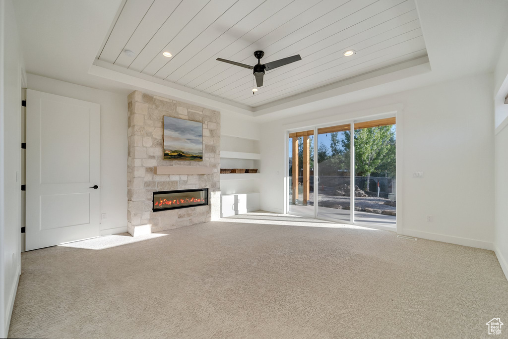 Unfurnished living room featuring a tray ceiling, a fireplace, wood ceiling, a ceiling fan, and carpet