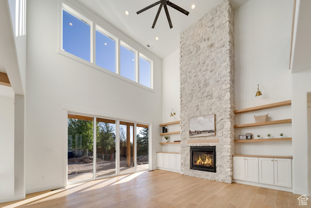 Unfurnished living room featuring a towering ceiling, a stone fireplace, light wood-style floors, plenty of natural light, and a ceiling fan