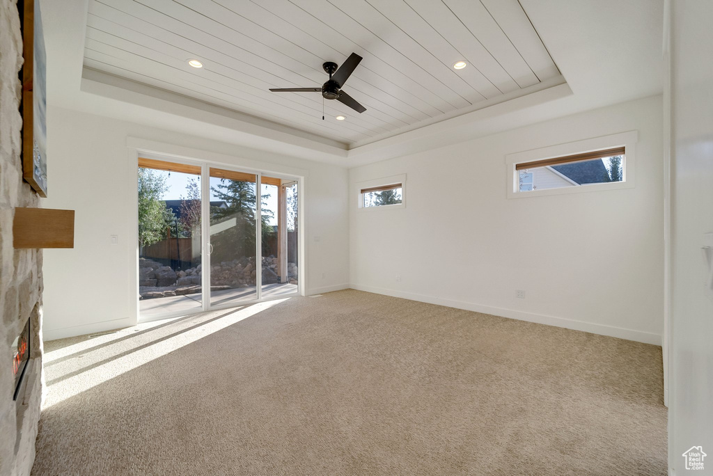 Spare room featuring a raised ceiling, a fireplace, carpet flooring, a ceiling fan, and wood ceiling