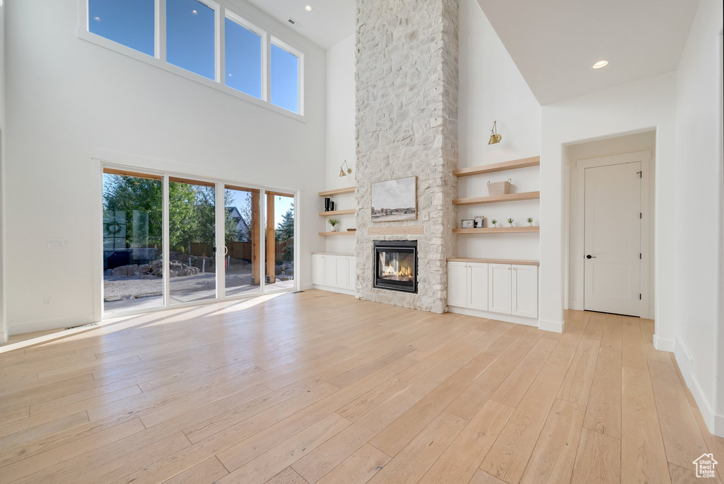 Unfurnished living room with a high ceiling, light wood-type flooring, a fireplace, and baseboards