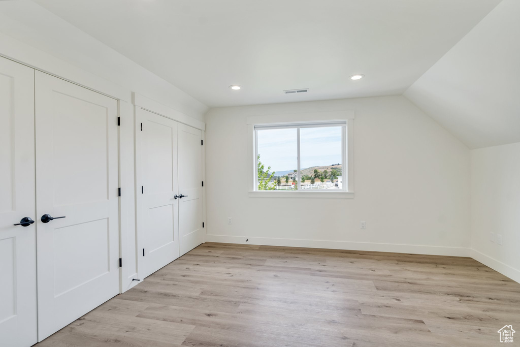 Unfurnished bedroom featuring multiple closets, light wood-style floors, recessed lighting, baseboards, and vaulted ceiling