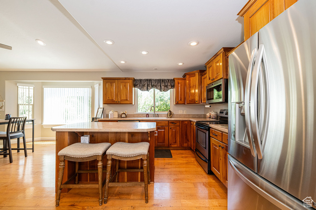 Kitchen with appliances with stainless steel finishes, brown cabinetry, light countertops, recessed lighting, and a sink
