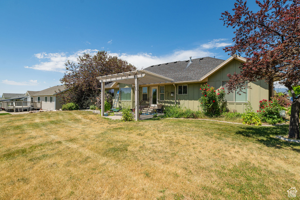 Rear view of property featuring a pergola, board and batten siding, a patio, a lawn, and roof with shingles