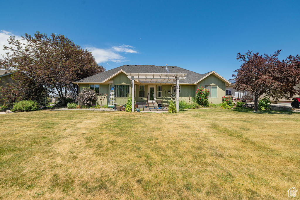 Rear view of property featuring a pergola, board and batten siding, a patio area, and a lawn