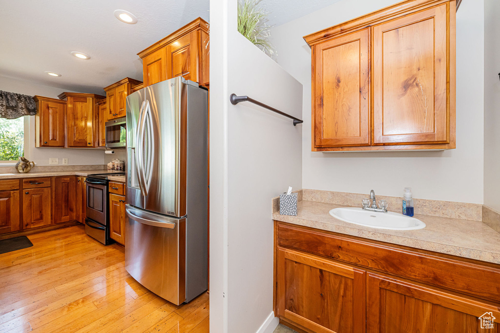 Kitchen with appliances with stainless steel finishes, light countertops, a sink, light wood-style flooring, and brown cabinets