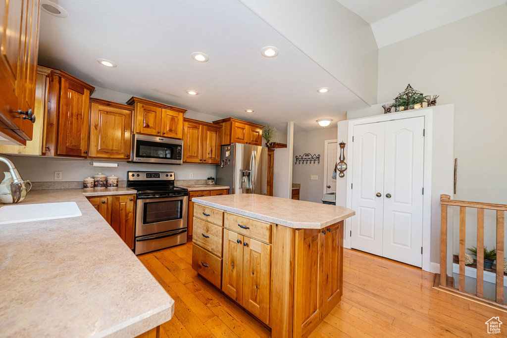 Kitchen with stainless steel appliances, a sink, light countertops, a kitchen island, and light wood-type flooring