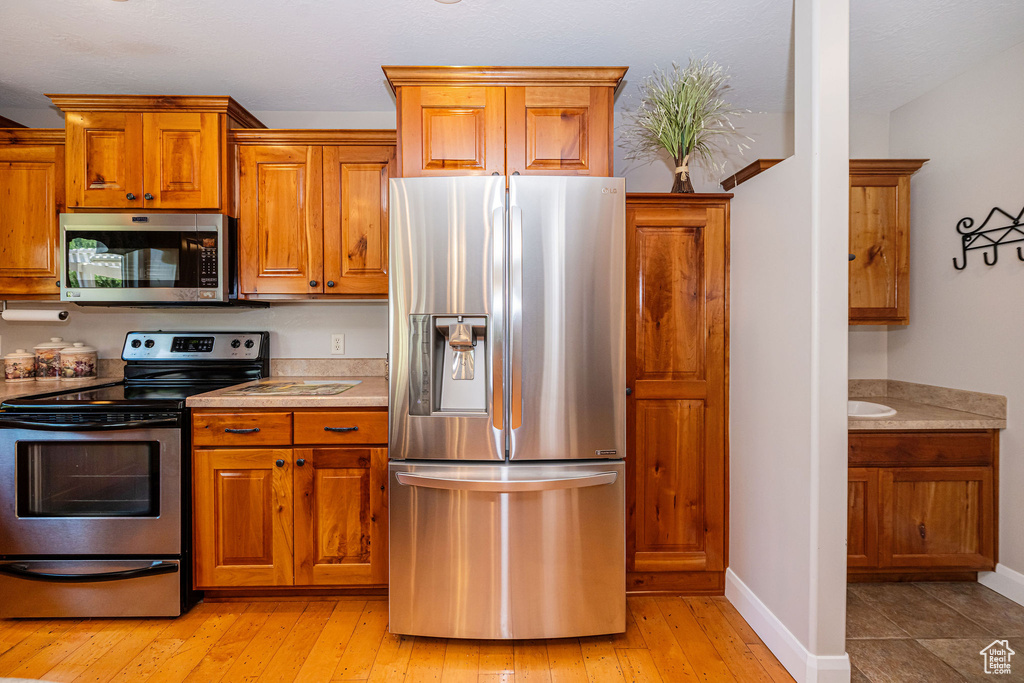 Kitchen with stainless steel appliances, light countertops, brown cabinetry, and light wood-style floors