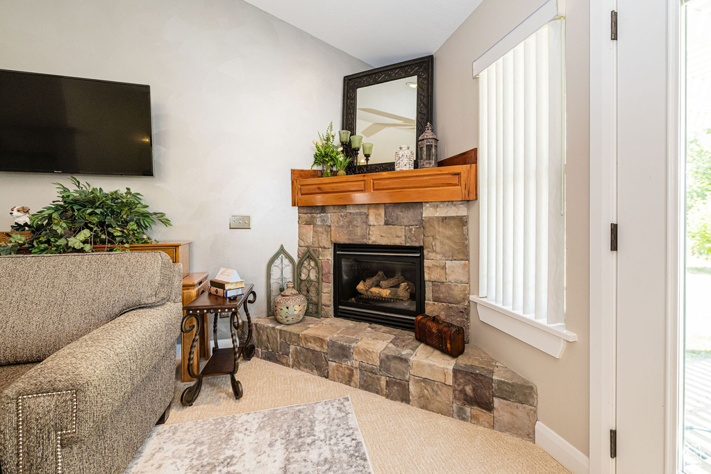 Carpeted living area featuring a stone fireplace and baseboards