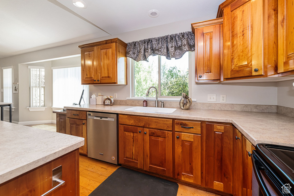 Kitchen featuring dishwasher, a sink, brown cabinets, black range with electric cooktop, and light countertops
