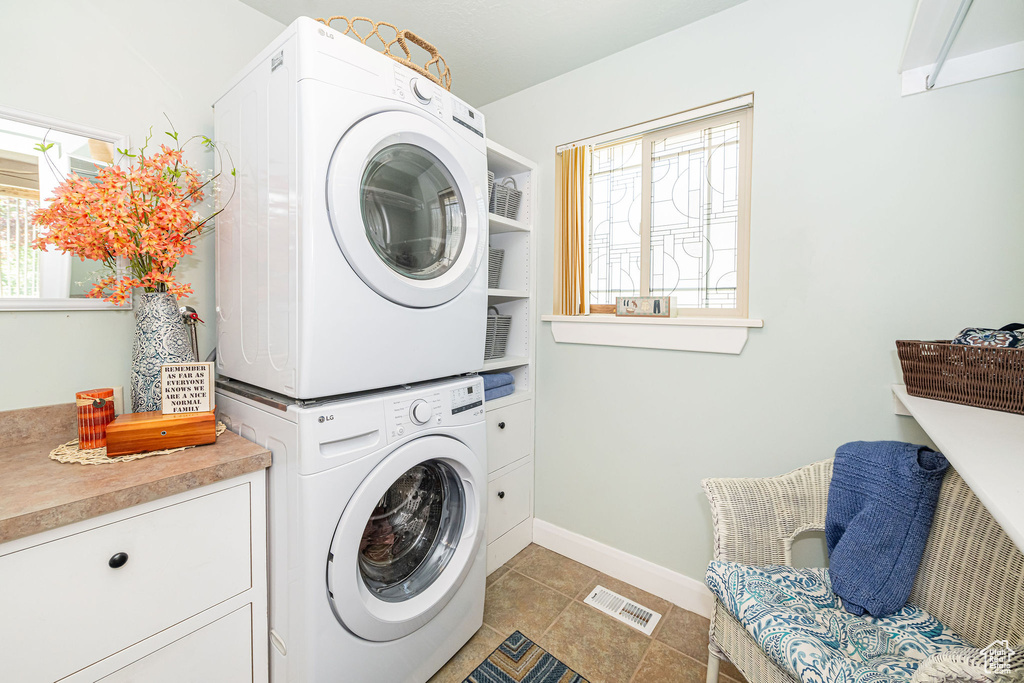 Laundry area with estacked washer and dryer, cabinet space, baseboards, and light tile patterned flooring
