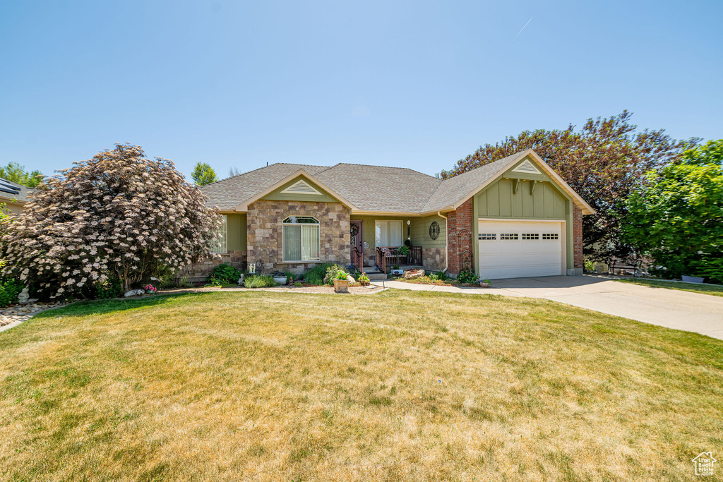 Single story home featuring driveway, board and batten siding, a garage, and a front lawn