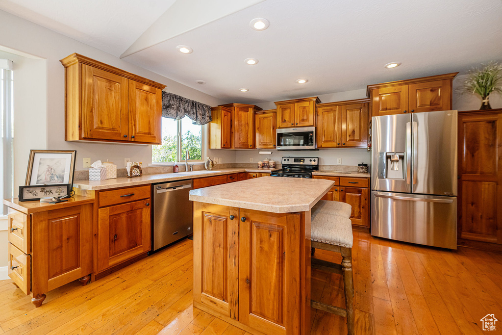 Kitchen with appliances with stainless steel finishes, a sink, light countertops, brown cabinetry, and recessed lighting