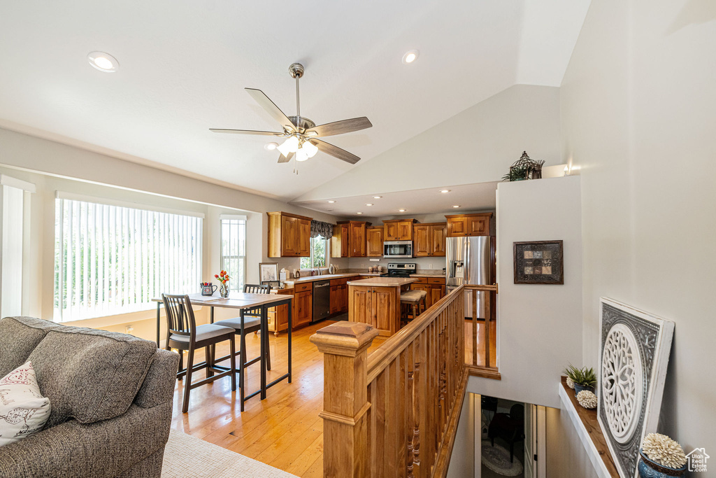 Kitchen with stainless steel appliances, a center island, brown cabinetry, light wood-type flooring, and a ceiling fan