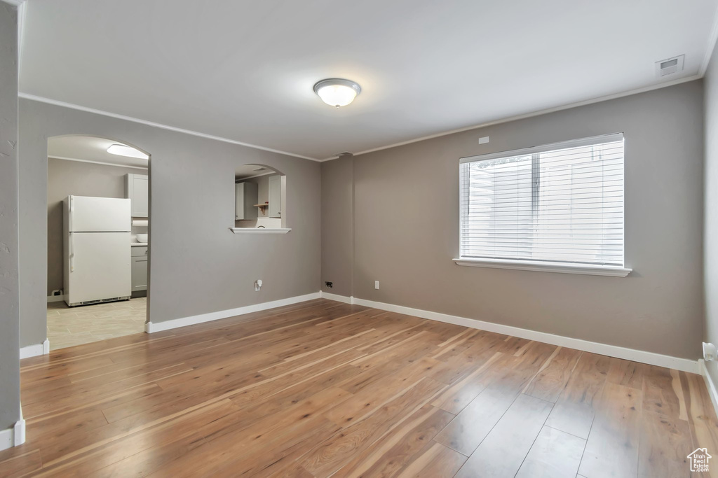 Empty room with baseboards, crown molding, light wood-style flooring, and arched walkways