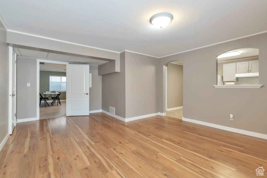 Empty room with arched walkways, light wood finished floors, baseboards, and ornamental molding