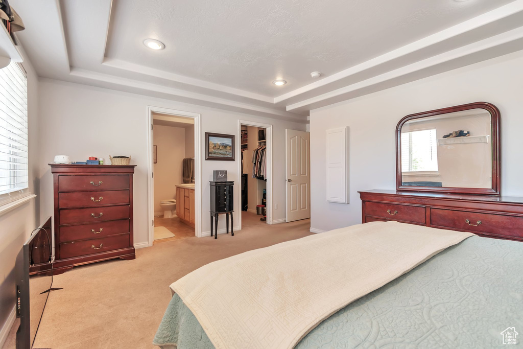 Bedroom with a raised ceiling, multiple windows, light colored carpet, a spacious closet, and recessed lighting