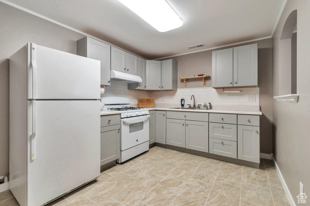 Kitchen featuring white appliances, a sink, gray cabinets, under cabinet range hood, and light countertops