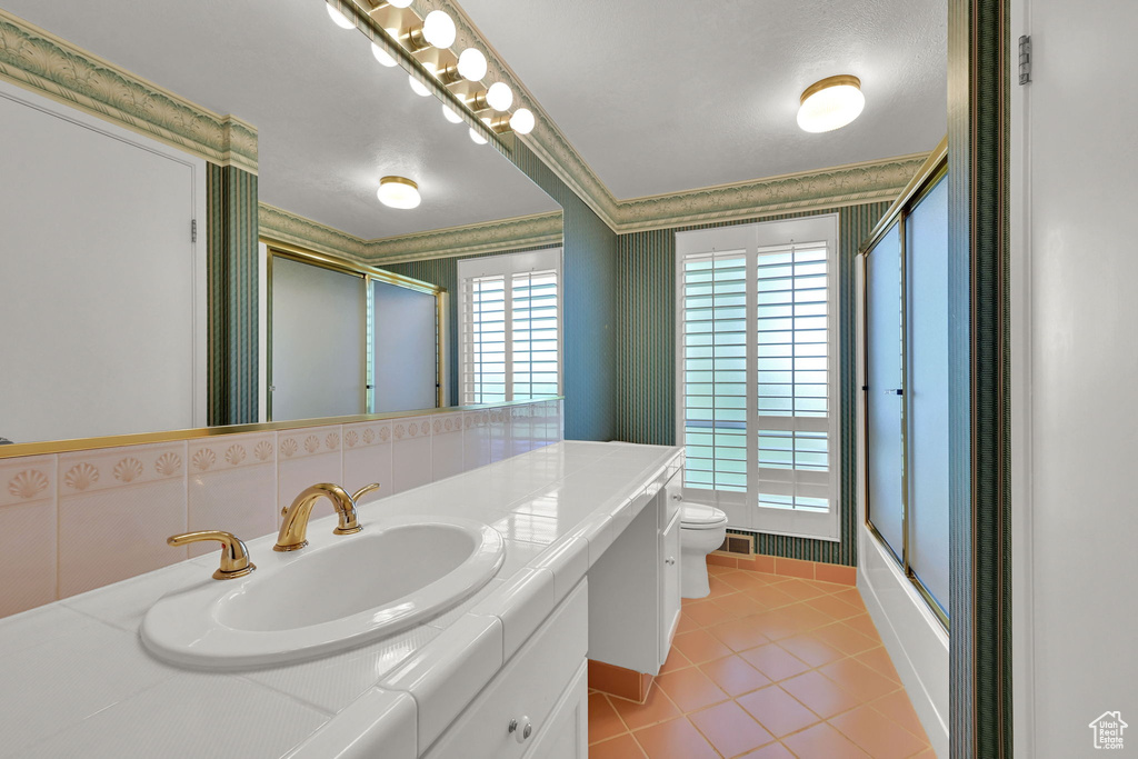Full bath featuring toilet, crown molding, vanity, tile patterned floors, and wallpapered walls