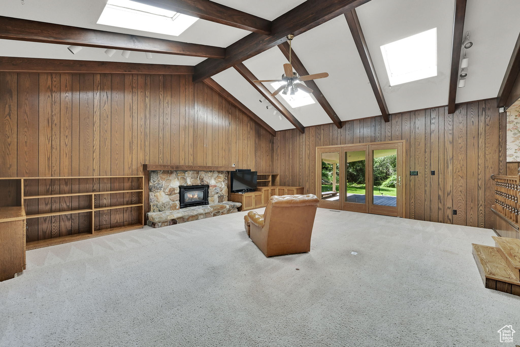 Carpeted living area featuring a skylight, wooden walls, ceiling fan, and a stone fireplace