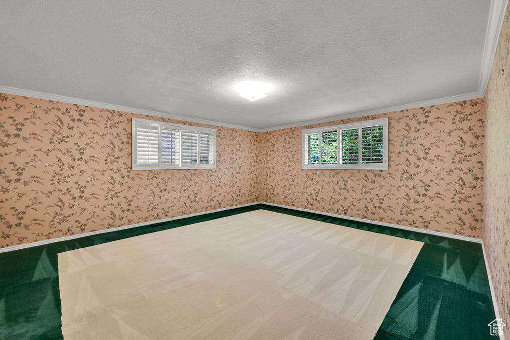 Spare room featuring carpet, wallpapered walls, ornamental molding, and a textured ceiling