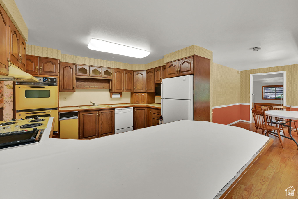 Kitchen with white appliances, light wood-style flooring, a peninsula, and light countertops
