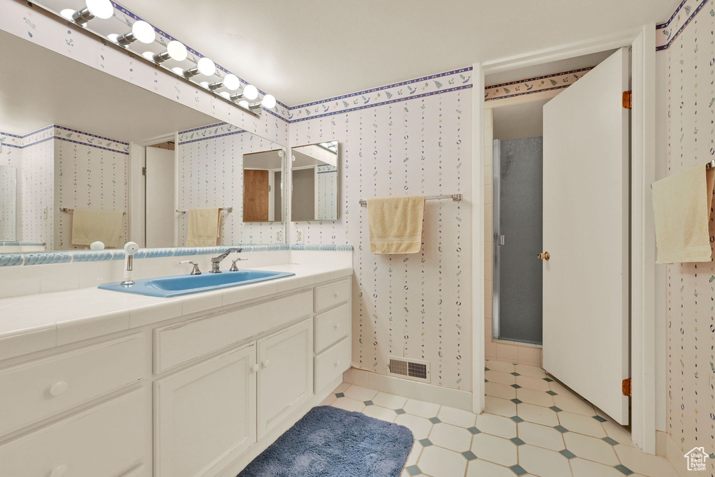 Bathroom featuring vanity, wallpapered walls, tile patterned floors, and a shower with shower door