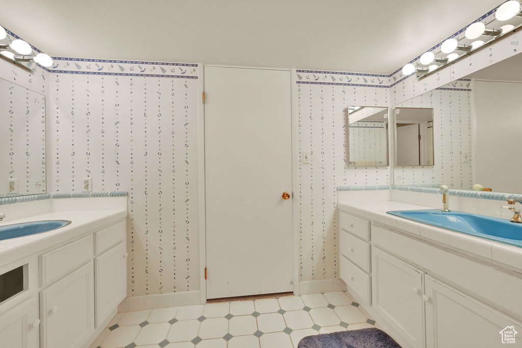 Bathroom with two vanities, baseboards, wallpapered walls, and tile patterned floors