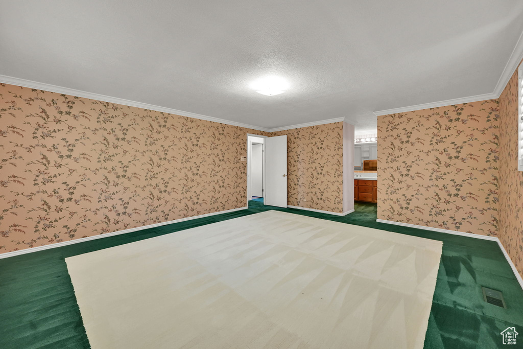 Unfurnished bedroom featuring wallpapered walls, ornamental molding, dark carpet, and baseboards