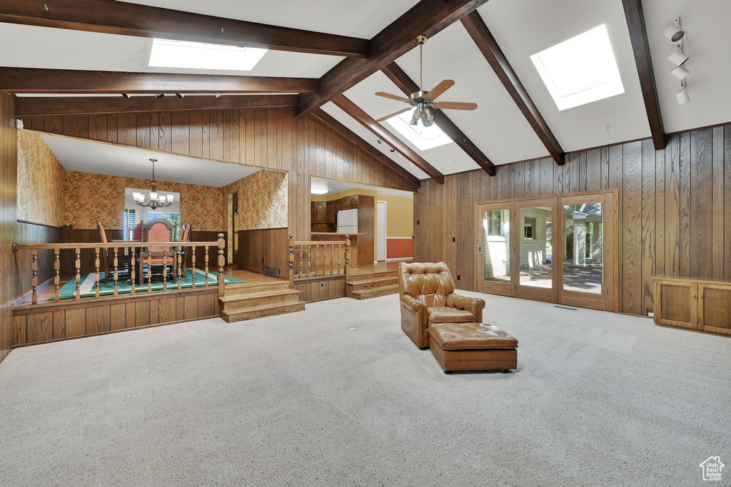 Living room with a skylight, wooden walls, a chandelier, carpet floors, and a ceiling fan
