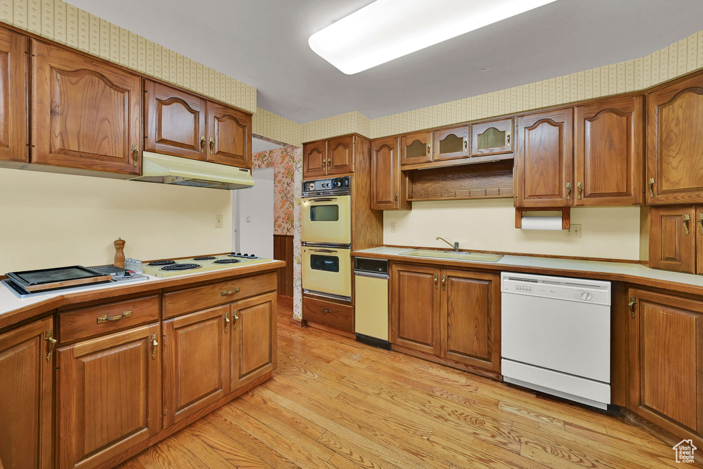 Kitchen with white appliances, under cabinet range hood, wallpapered walls, light wood-style floors, and brown cabinets