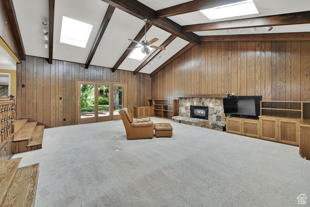 Living room with a skylight, wood walls, a stone fireplace, ceiling fan, and carpet floors