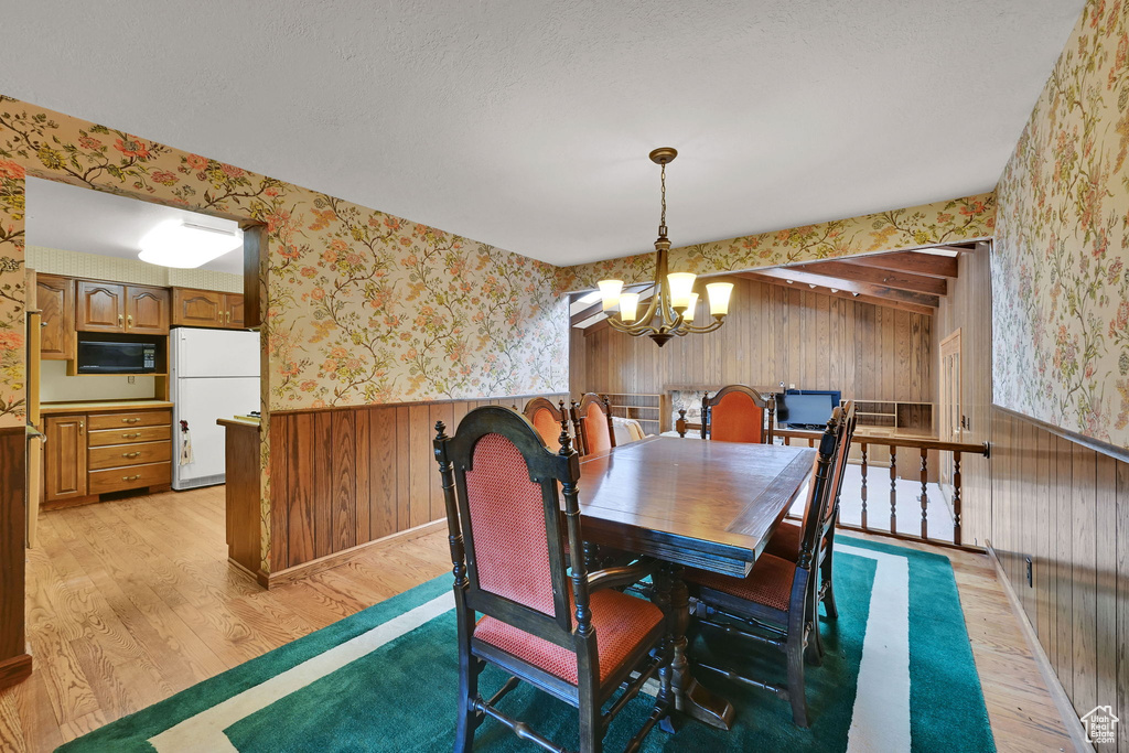 Dining room with wallpapered walls, light wood finished floors, a chandelier, wainscoting, and wooden walls