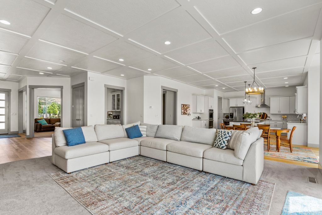 Living area featuring coffered ceiling, light colored carpet, recessed lighting, and a chandelier