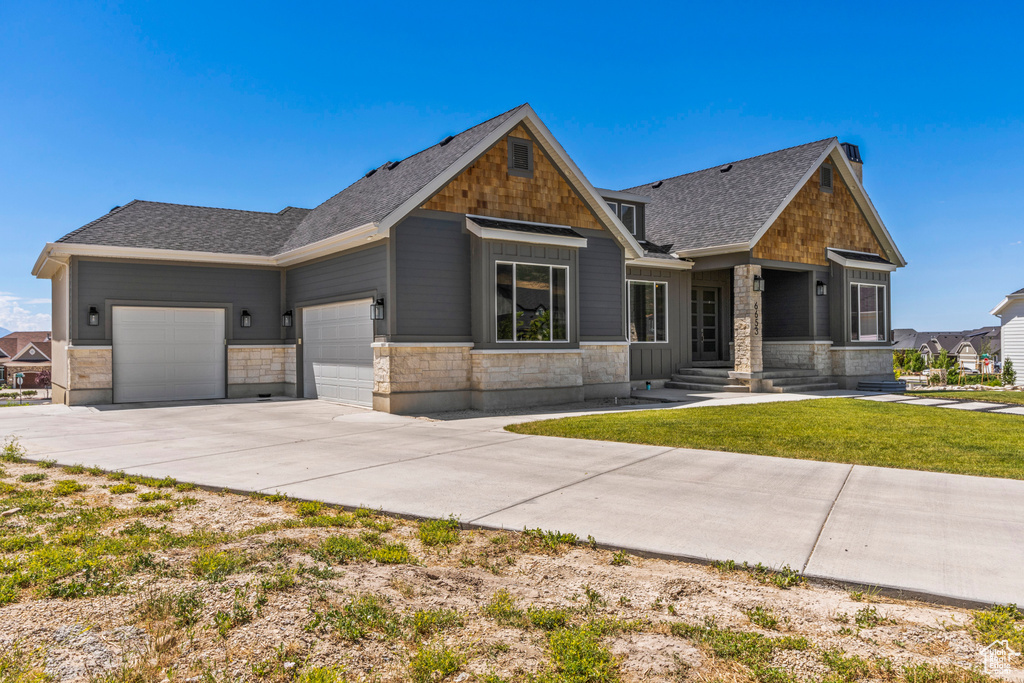 Craftsman inspired home with a garage, concrete driveway, a shingled roof, a front yard, and stone siding
