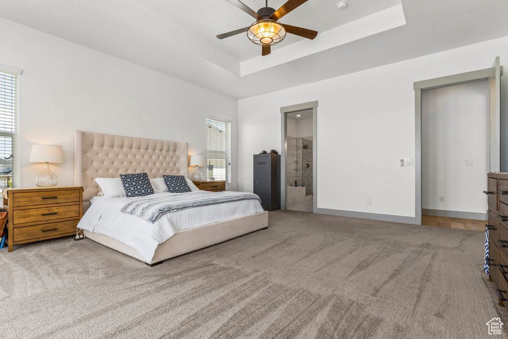 Bedroom featuring carpet floors, a tray ceiling, ensuite bathroom, and a ceiling fan