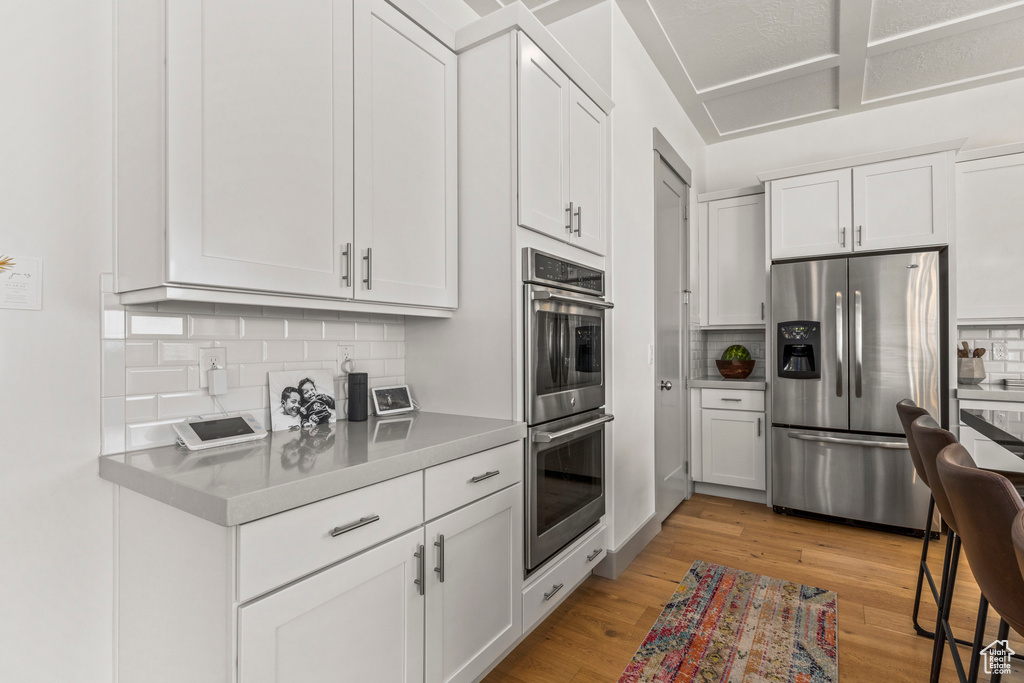 Kitchen with stainless steel appliances, tasteful backsplash, light countertops, and light wood-style floors