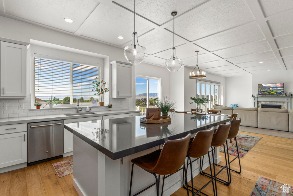 Kitchen featuring stainless steel dishwasher, a sink, backsplash, a kitchen bar, and light wood-type flooring