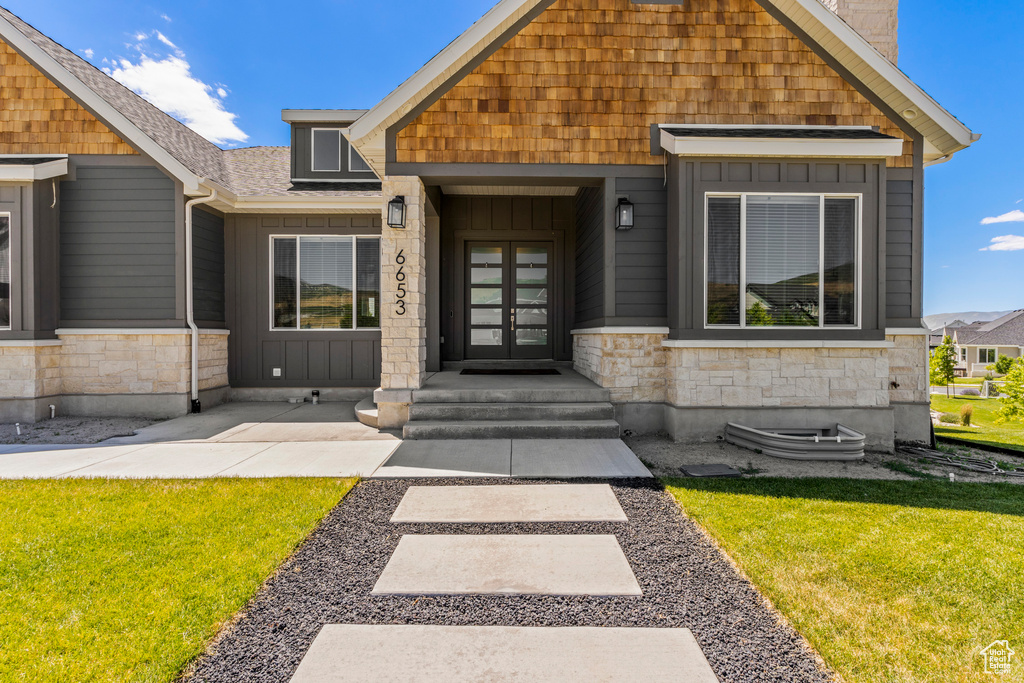 View of front of home with french doors, stone siding, a front lawn, and board and batten siding