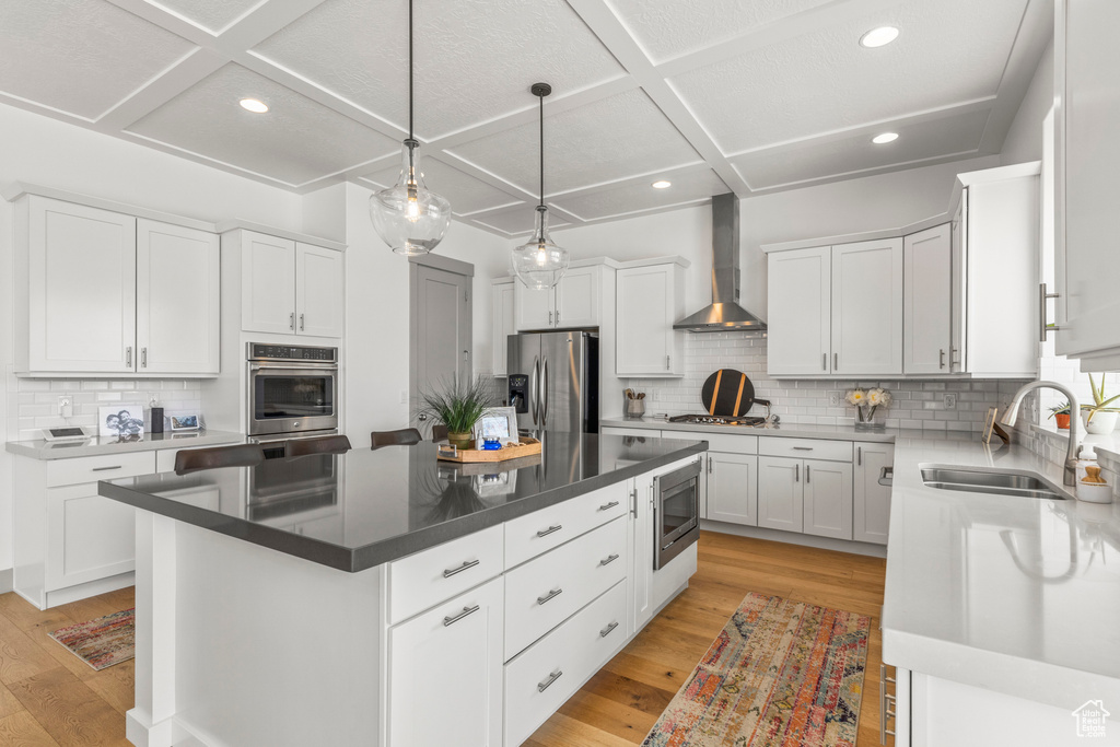Kitchen featuring stainless steel appliances, wall chimney range hood, coffered ceiling, a sink, and backsplash